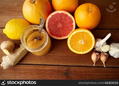 traditional medicine, cooking, food and ethnoscience concept - honey, citrus fruits with ginger and garlic on wooden background
