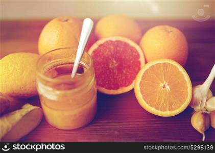 traditional medicine, cooking, food and ethnoscience concept - honey, citrus fruits with ginger and garlic on wooden table. honey, citrus fruits, ginger and garlic on wood