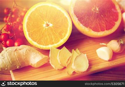 traditional medicine, cooking, food and ethnoscience concept - orange, grapefruit with ginger and garlic on wooden board. citrus, ginger, garlic and rowanberry on wood
