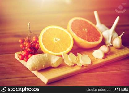 traditional medicine, cooking, food and ethnoscience concept - orange, grapefruit with ginger and garlic on wooden board. citrus, ginger, garlic and rowanberry on wood