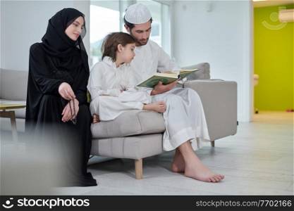 Traditional muslim family parents with children reading Quran and praying together on the sofa before iftar dinner during a ramadan feast at home