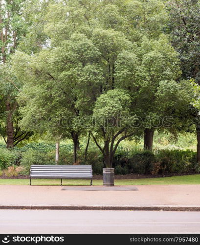 Traditional Park Bench with Litter Trash Bin in Green park with Pavement Sidewalk