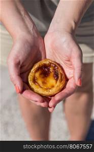Traditional Portuguese egg tart pasty cake dessert Pasteis de nata in women hand. On background attractions in Lisbon, Portugal.