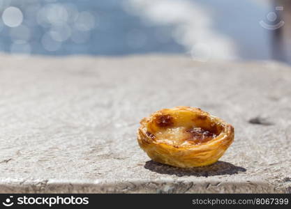 Traditional Portuguese egg tart pasty cake dessert Pasteis de nata on background seafront in Lisbon, Portugal.