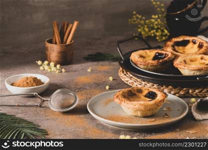 Traditional Portuguese pastry Pastel de Nata or Pastel de Belem served with cinnamon powder in a traditional tray on a rustic board. Egg tart