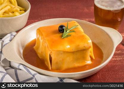 Traditional Portuguese snack food. Francesinha sandwich of bread, cheese, pork, ham, sausages, with tomato beer sauce and French fries. With beer and potatoes. On table.