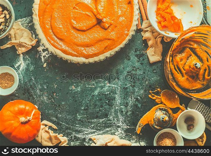 Traditional pumpkin pie preparation with filling, dough and ingredients on dark rustic background, top view, retro styled, frame