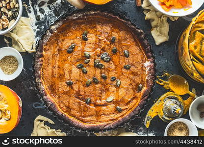 Traditional pumpkin pie with seeds and ingredients on dark rustic background, top view, retro styled