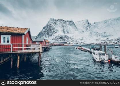 Traditional red rorbu houses in Reine fishing village in winter and pier with boats. Lofoten islands, Norway. Traditional red rorbu houses in Reine, Norway