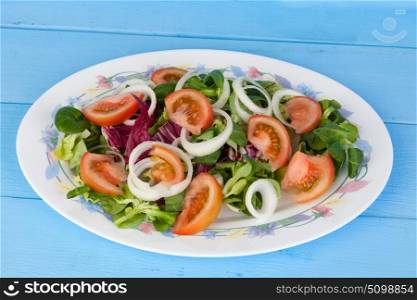 Traditional salad with tomato, lettuce and onion on a wooden blue table.