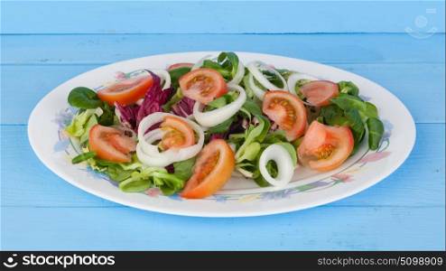 Traditional salad with tomato, lettuce and onion on a wooden blue table.