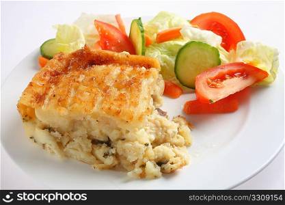 Traditional seafood pie, with fish in bechamel sauce topped with mashed potato and baked, served with a salad, side view