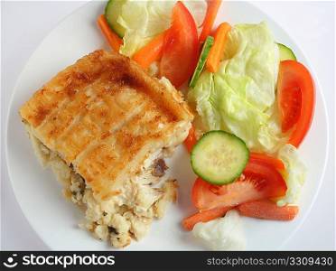 Traditional seafood pie, with fish in bechamel sauce topped with mashed potato and baked, served with a salad, high angle view
