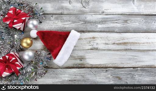 Traditional silver and gold balls, Santa hat plus presents surrounded by tinsel on a white wood background for the Christmas or New Year holiday season