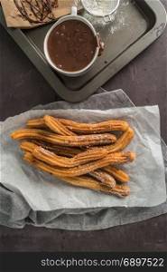 Traditional Spanish and Mexican dessert churros with hot chocolate sauce on black stone background.