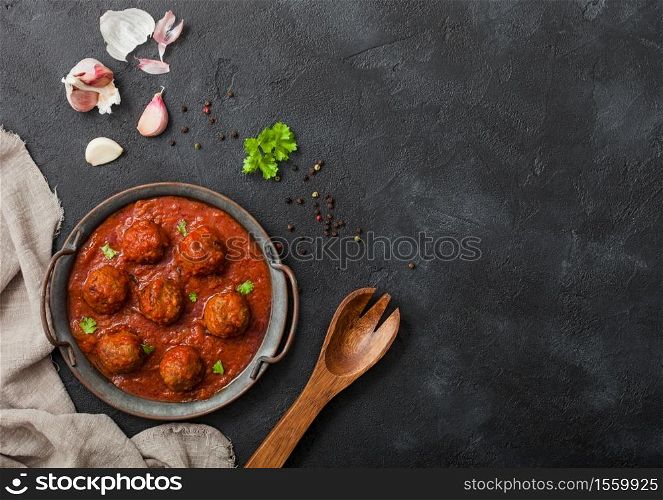 Traditional spicy meatballs in tomato sauce with pepper, garlic and parsley on black background. Space for text