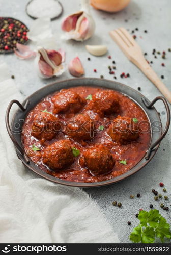 Traditional spicy meatballs in tomato sauce with pepper, garlic and parsley on light table.