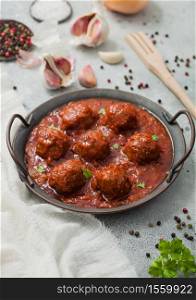 Traditional spicy meatballs in tomato sauce with pepper, garlic and parsley on light table.