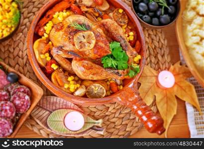 Traditional Thanksgiving day dinner, tasty roasted turkey, cold cuts, corn and olives on the festive table decorated with dry maple leaves and candles