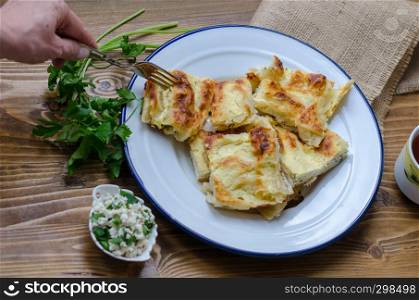 Traditional turkish borek in a enamel dish on wooden table.