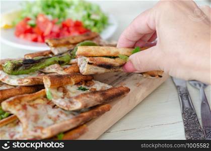 Traditional Turkish cuisine : Pita(pide) with minced meat and cheese, close up.The woman is eating the pita.