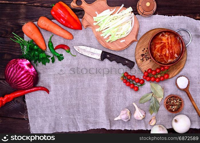 Traditional Ukrainian borsch in a brown clay dish with vegetables ingredients, empty space in the middle