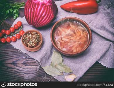 Traditional Ukrainian borsch in a round brown plate in the middle of vegetables and ingredients on a wooden table, top view