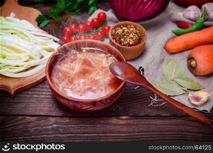 Traditional Ukrainian borsch in a round brown plate in the middle of vegetables and ingredients on a wooden table