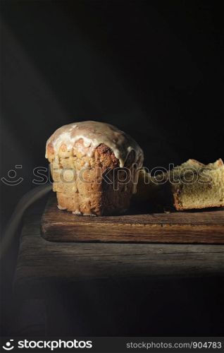 traditional Ukrainian Easter pastry lies on a wooden board, black background, rays of the sun from the window