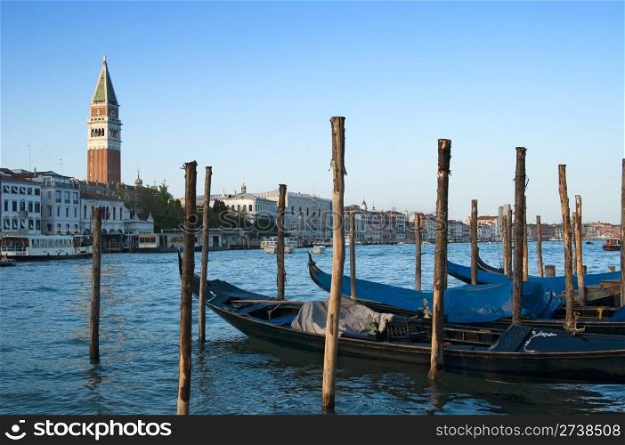 Traditional venetian gondlolas and St Mark&rsquo;s Campanile over blue sky in Venice, Italy