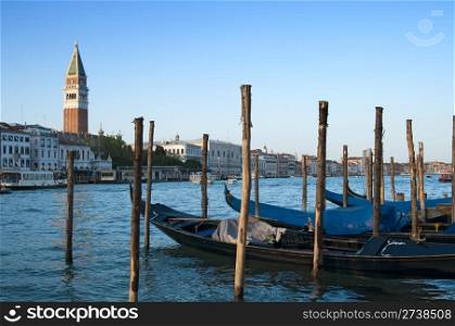 Traditional venetian gondlolas and St Mark&rsquo;s Campanile over blue sky in Venice, Italy