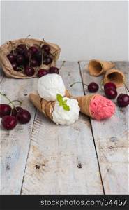 Traditional waffle cones for ice cream on wooden table. Cherry ice cream and fresh cherries. Cones filled with ice cream