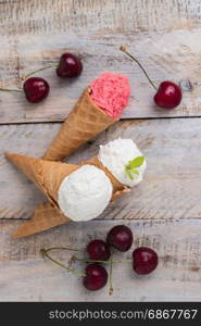 Traditional waffle cones for ice cream on wooden table. Cherry ice cream and fresh cherries. Cones filled with ice cream