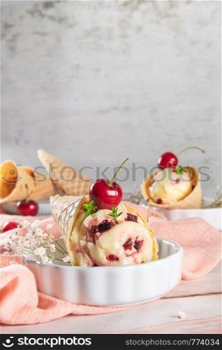 Traditional waffle cones with ice cream and cherry fruits on marble stone surface.