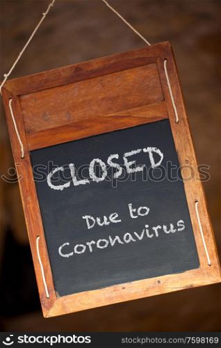 Traditional wooden blackboard or chalkboard sign hanging in a window saying Closed Due to Coronavirus