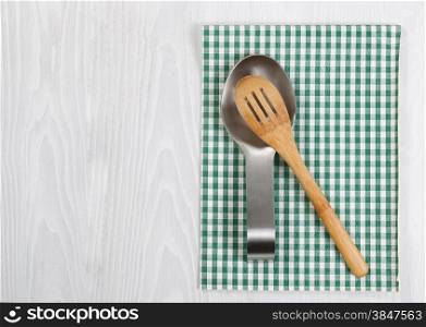 Traditional wooden spoon in stainless steel spoon rest with striped cloth napkin on white wood. Format in horizontal layout.