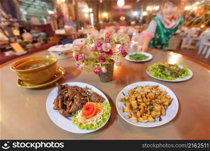 Traditional Yunnan-Chinese cuisine set, roasted chicken with sauce and salad, stir fried Chicken and cashew nut, mild soup and tea leaf salad, waitress serving in the background. Focus on plate.