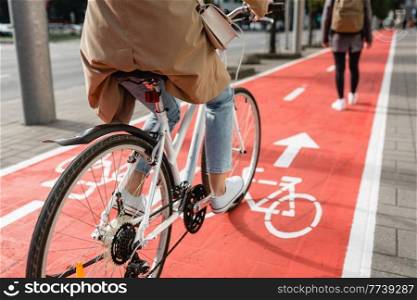 traffic, city transport and people concept - close up of woman cycling behind pedestrian walking along red bike lane or road with signs of bicycles on street. woman cycling behind pedestrian along bike lane