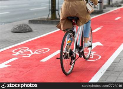 traffic, city transport and people concept - woman cycling along red bike lane with signs of bicycles on street. woman cycling along red bike lane road in city
