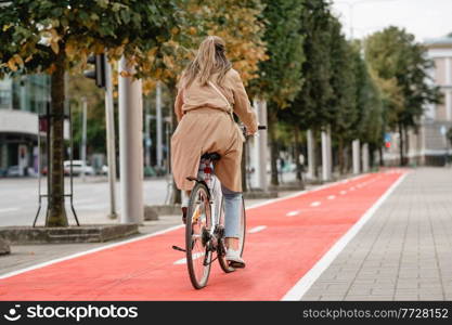 traffic, city transport and people concept - woman riding bicycle along red bike lane or two way road on street. woman riding bicycle along red bike lane in city