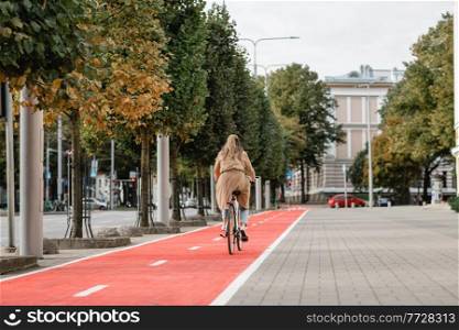 traffic, city transport and people concept - woman riding bicycle along red bike lane or two way road on street. woman riding bicycle along red bike lane in city