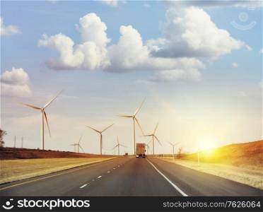 Traffic moves along an interstate highway with wind turbines at sunset