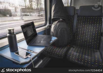 Train interior with comfortable chairs, a table, and a window view. Traveling by train concept with backpack and laptop on seats. Public transport.