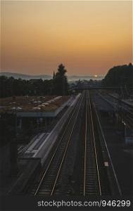 Train station and railroads at sunrise. Railway lines leading towards the horizon. Strong morning sun on the clean sky