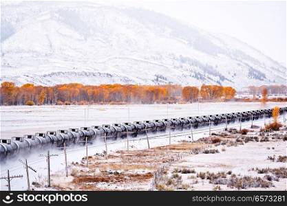Train transporting tank cars. Season changing, first snow and autumn trees. Rocky Mountains, Colorado, USA. 