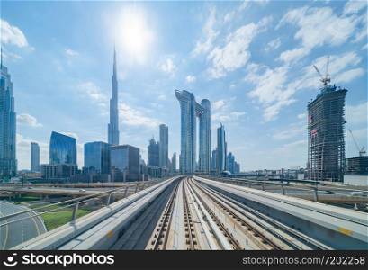 Train view on railway in Dubai Downtown at financial district, skyscraper buildings in urban city, UAE. Transportation for tourists visiting in travel trip or holiday vacation at noon with blue sky.