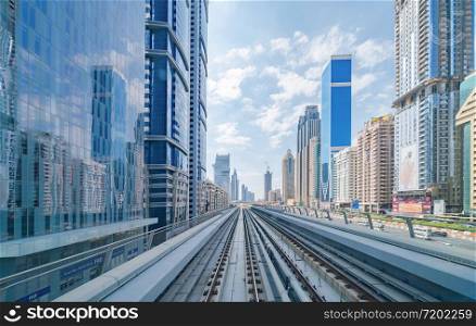 Train view on railway in Dubai Downtown at financial district, skyscraper buildings in urban city, UAE. Transportation for tourists visiting in travel trip or holiday vacation at noon with blue sky.