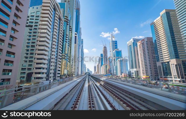 Train view on railway in Dubai Downtown at financial district, skyscraper buildings in urban city, UAE. Transportation for tourists visiting in travel trip or holiday vacation at noon with blue sky.