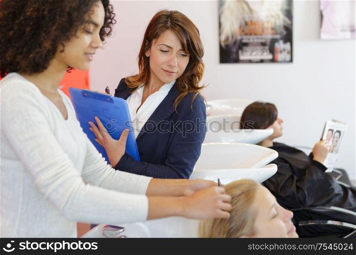 trainee hairdresser washing female clients hair under supervision