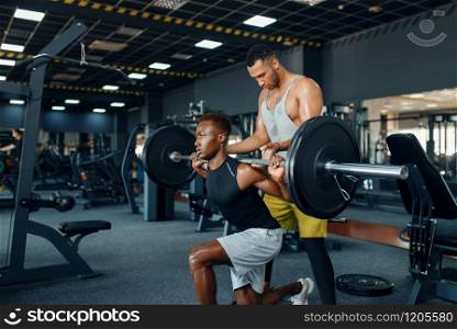 Trainer helps the athlete, exercise with barbell on training in gym. Workout in sport club, healthy lifestyle